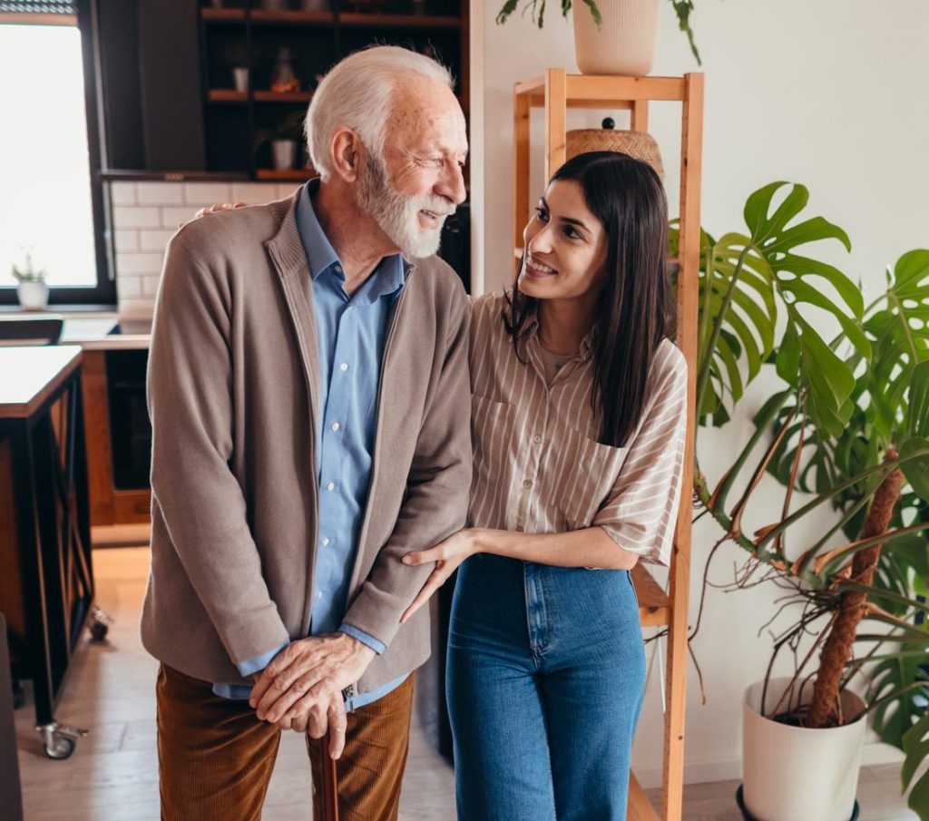 Young woman assisting elderly man with cane at home