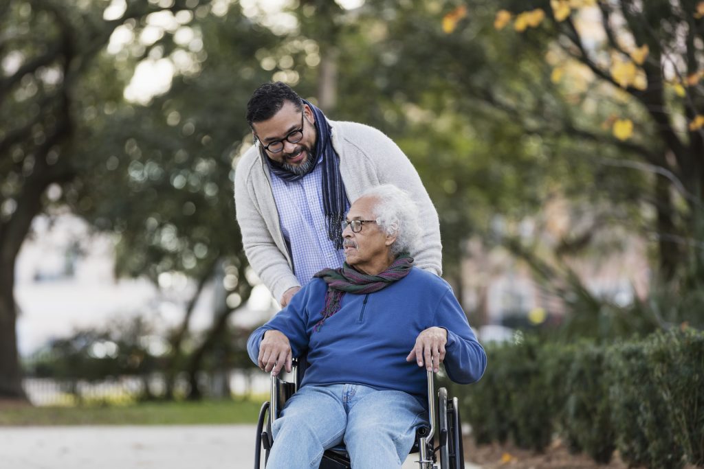 Senior man in wheelchair being pushed by this son