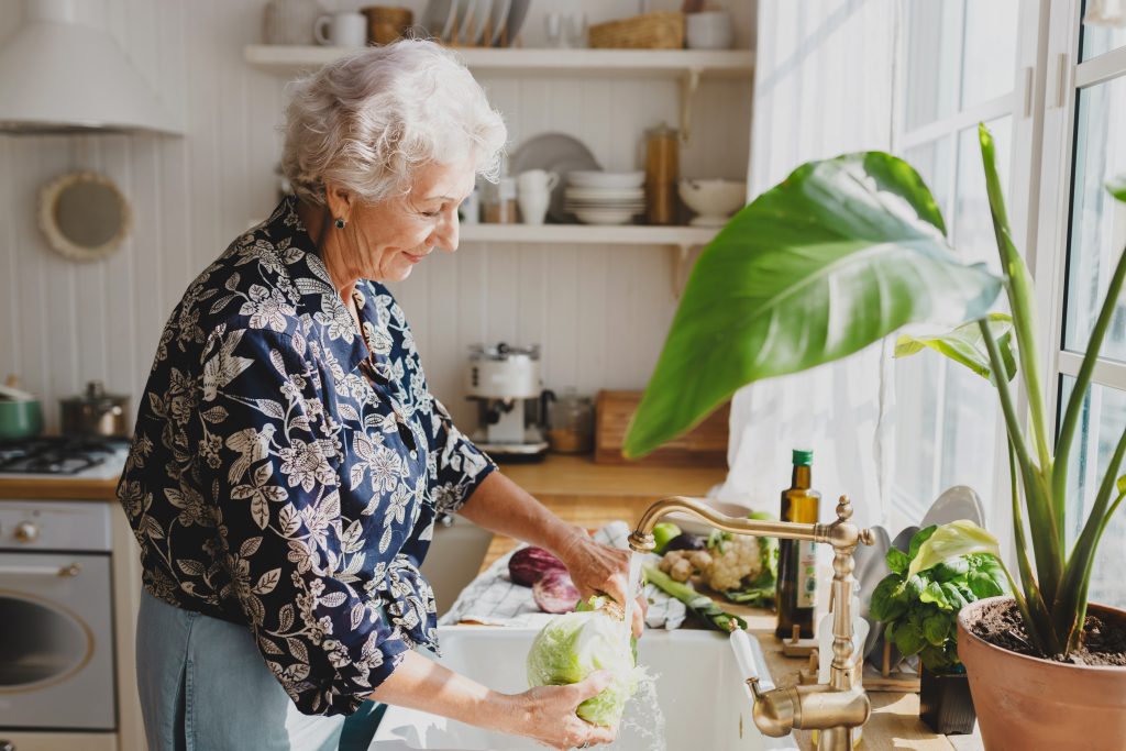 elderly woman washing lettuce in her sink